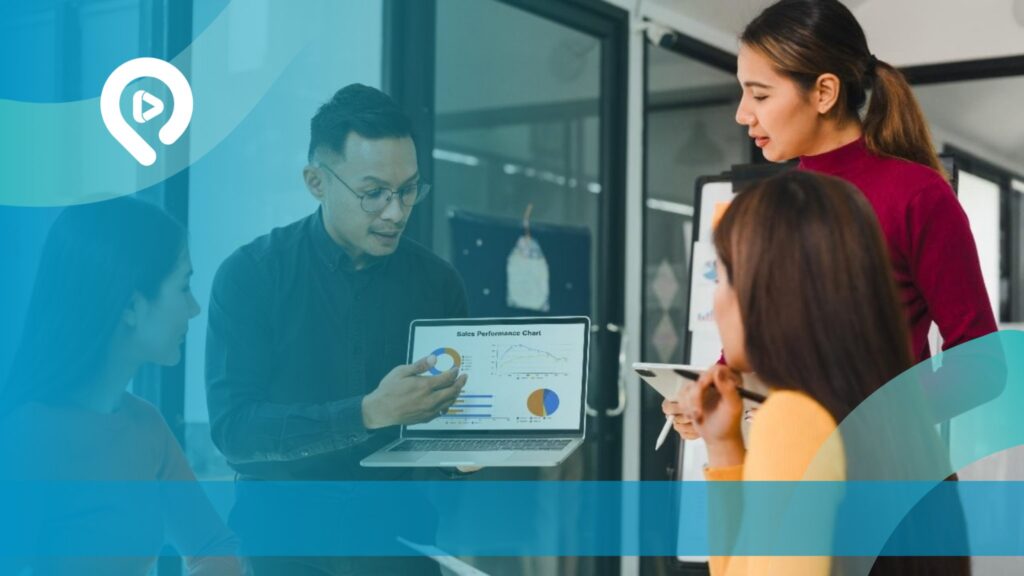 Tim sales B2B sedang berdiskusi mengenai kinerja penjualan menggunakan laptop yang menampilkan grafik, dalam suasana rapat di kantor.