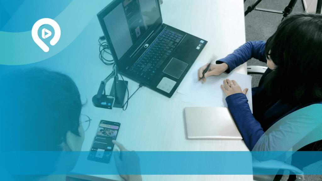 Dua orang bekerja di depan laptop dan menggunakan ponsel di meja kerja dengan desain visual bernuansa biru dan logo layanan digital.