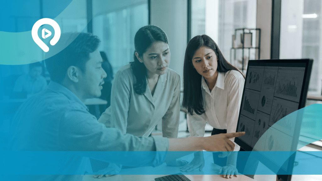 Tiga orang profesional berdiskusi sambil menganalisis grafik dan data penjualan pada layar monitor untuk mendukung strategi bisnis berbasis GEO-Sales Automation System.
